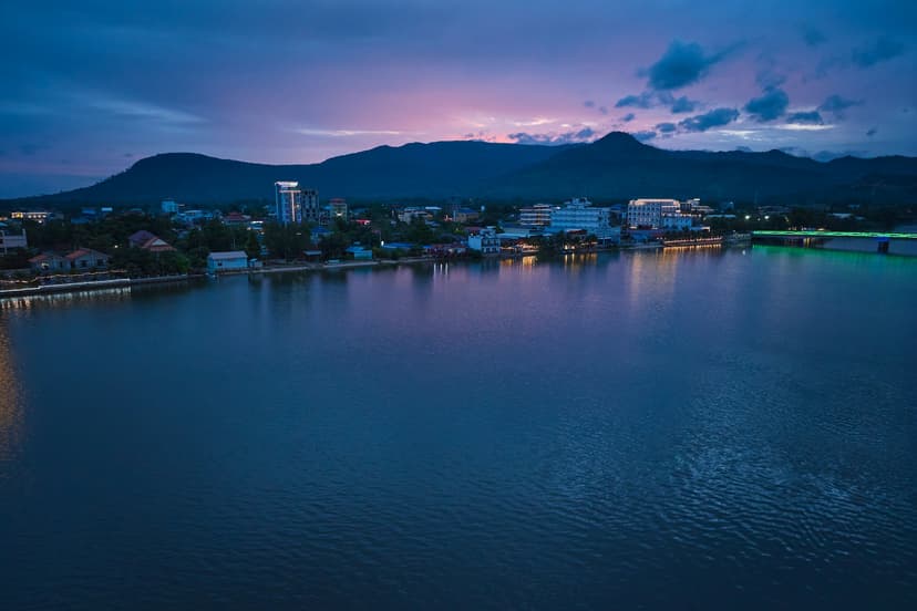 Illuminated riverside buildings at dusk with mountains behind