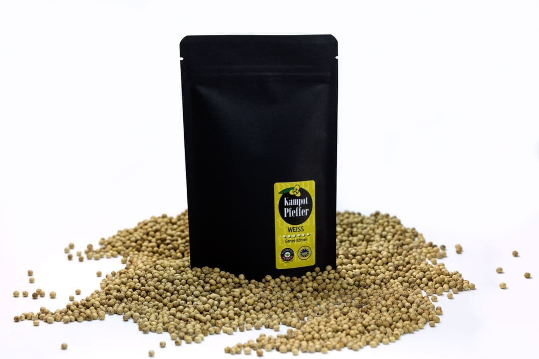 Black stand-up pouch of Kampot white pepper on scattered white peppercorns