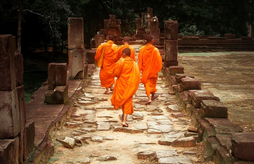 Buddhist monks in saffron robes walking through ancient Angkor temple ruins